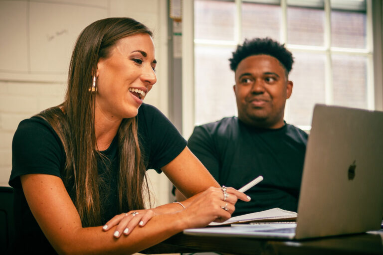 woman laughing pointing at laptop next to man