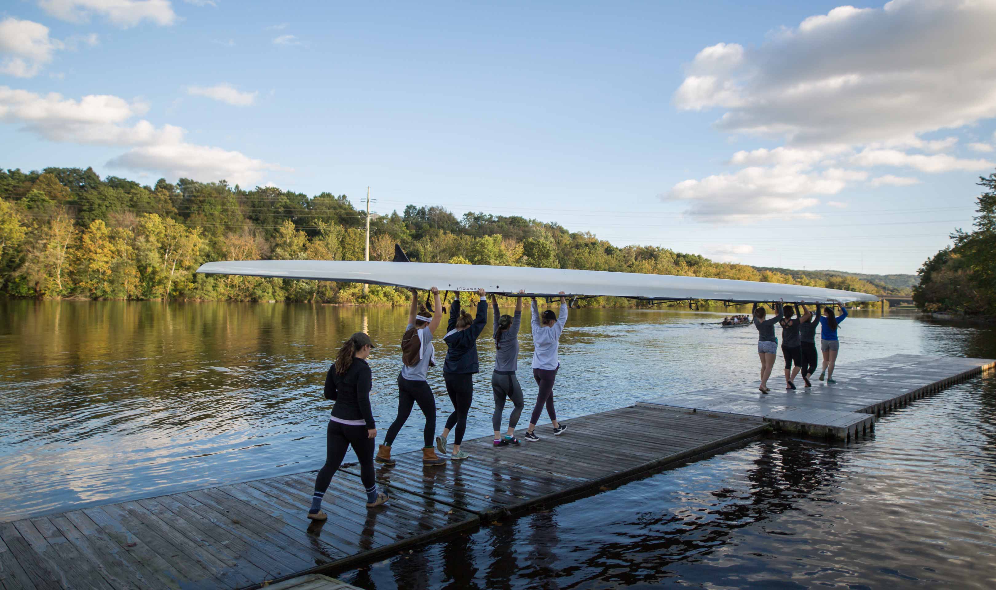 Students are collectively moving a rowing boat on the river floating deck.