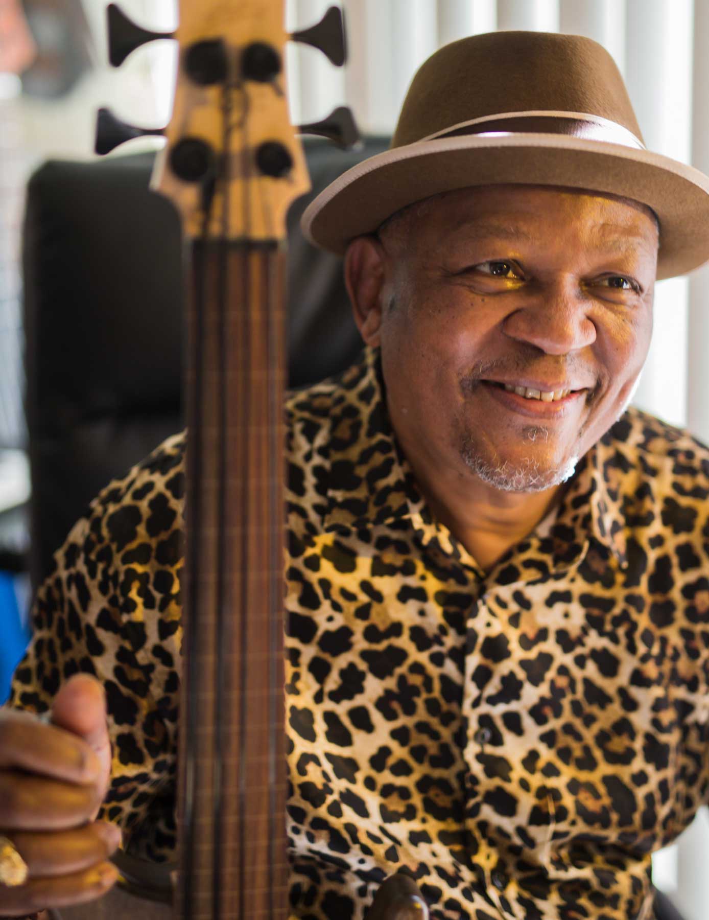 A man wearing a fedora is smiling while holding a string instrument.