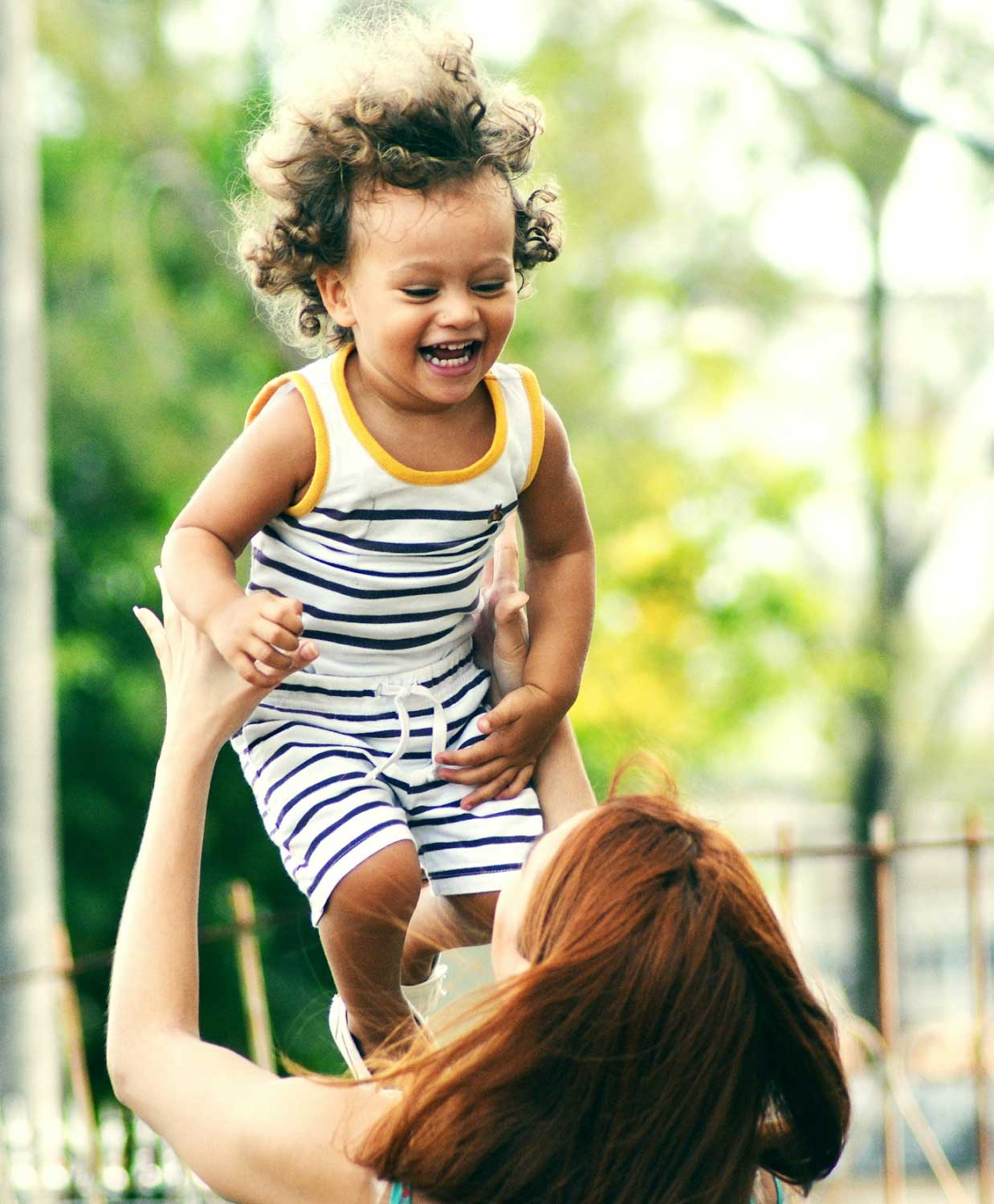 A mother is lifting a smiling child up into the sky.