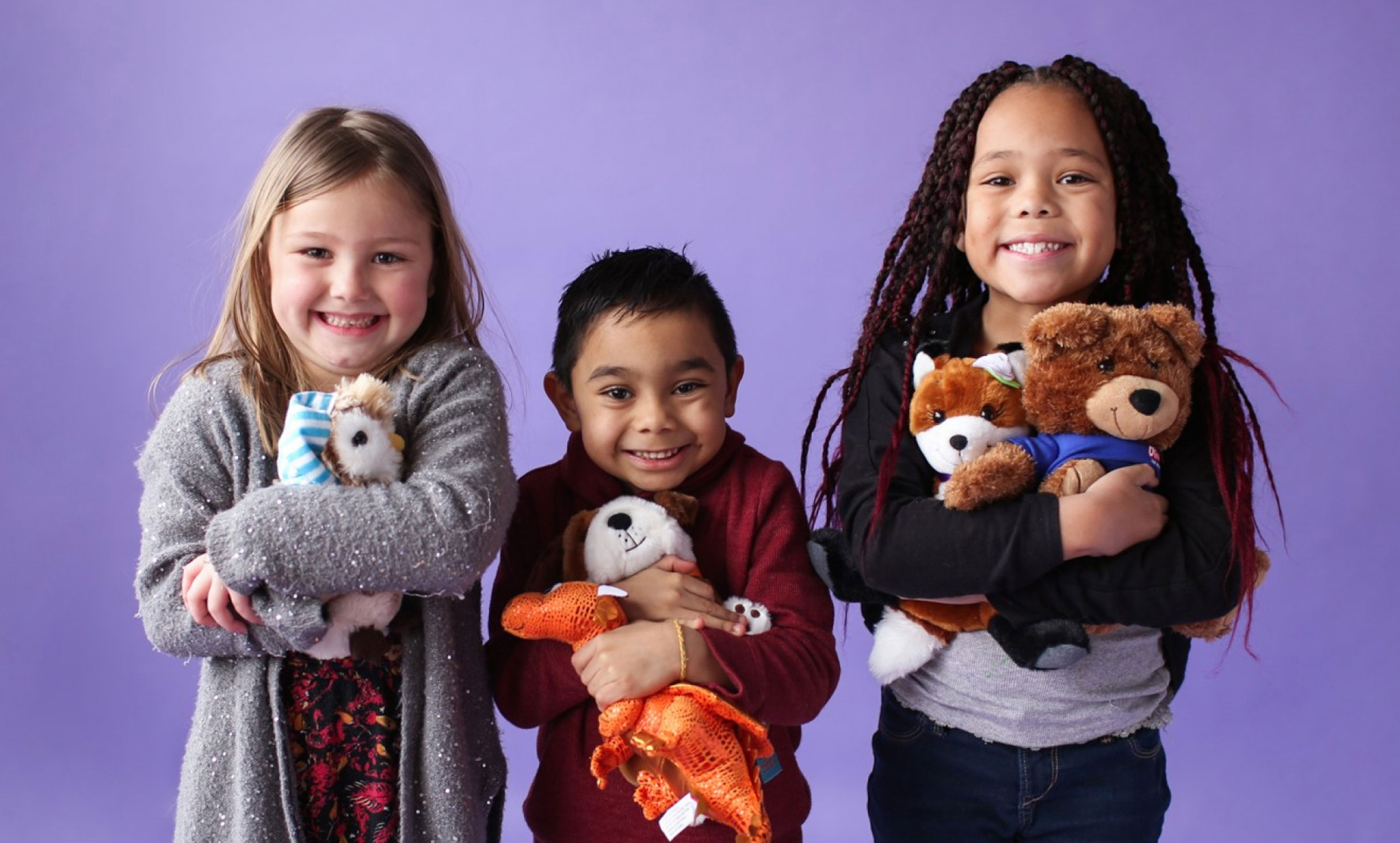 Three kids smiling at the camera while holding teddy bears