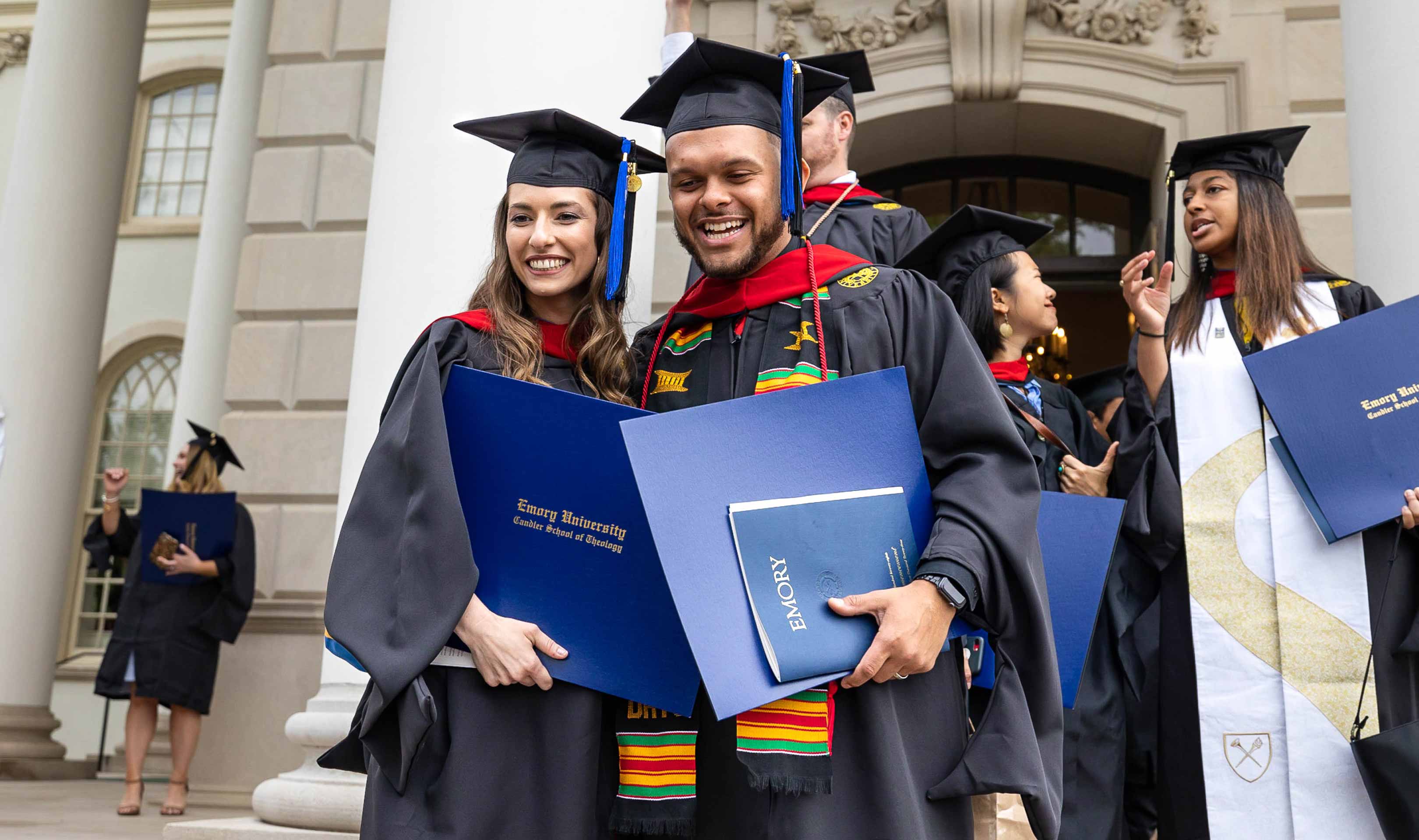 A man and a woman are smiling at the camera, wearing graduation gowns and caps.