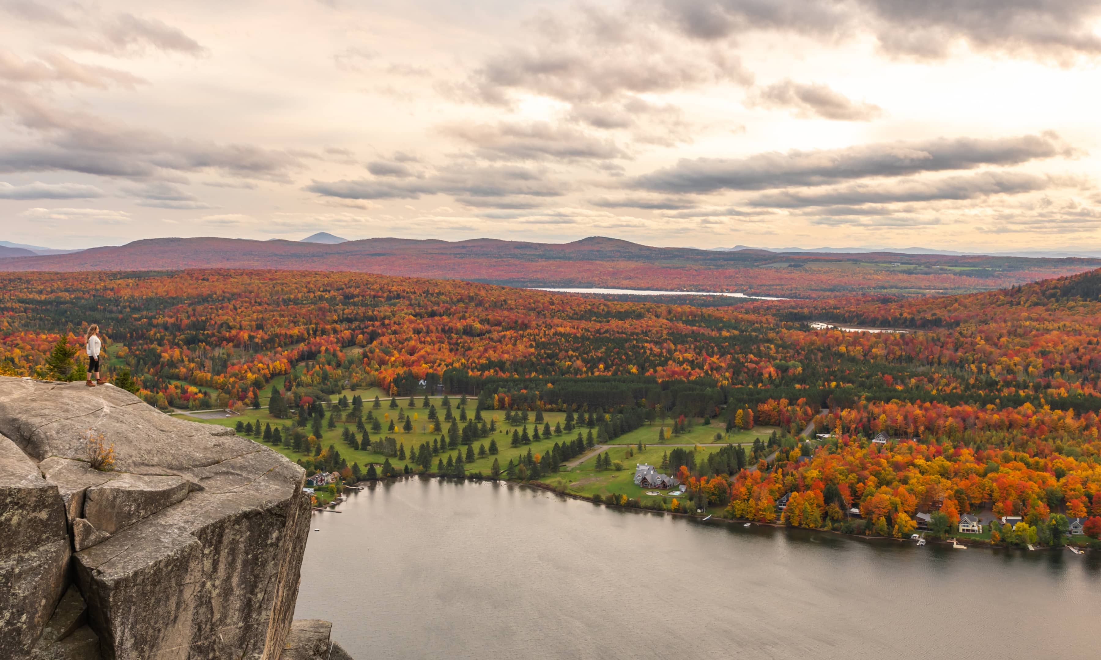 A woman standing on a mountain cliff overlooking a scenic view of rural Vermont