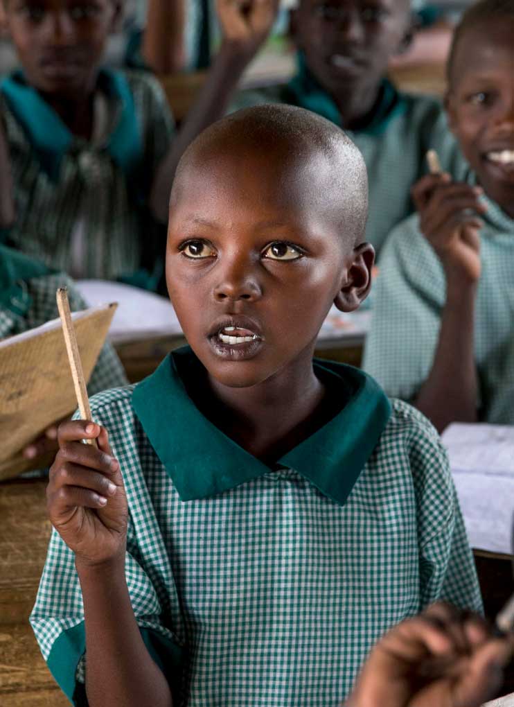 A girl is sitting at a desk, holding a wooden stick, and saying something.