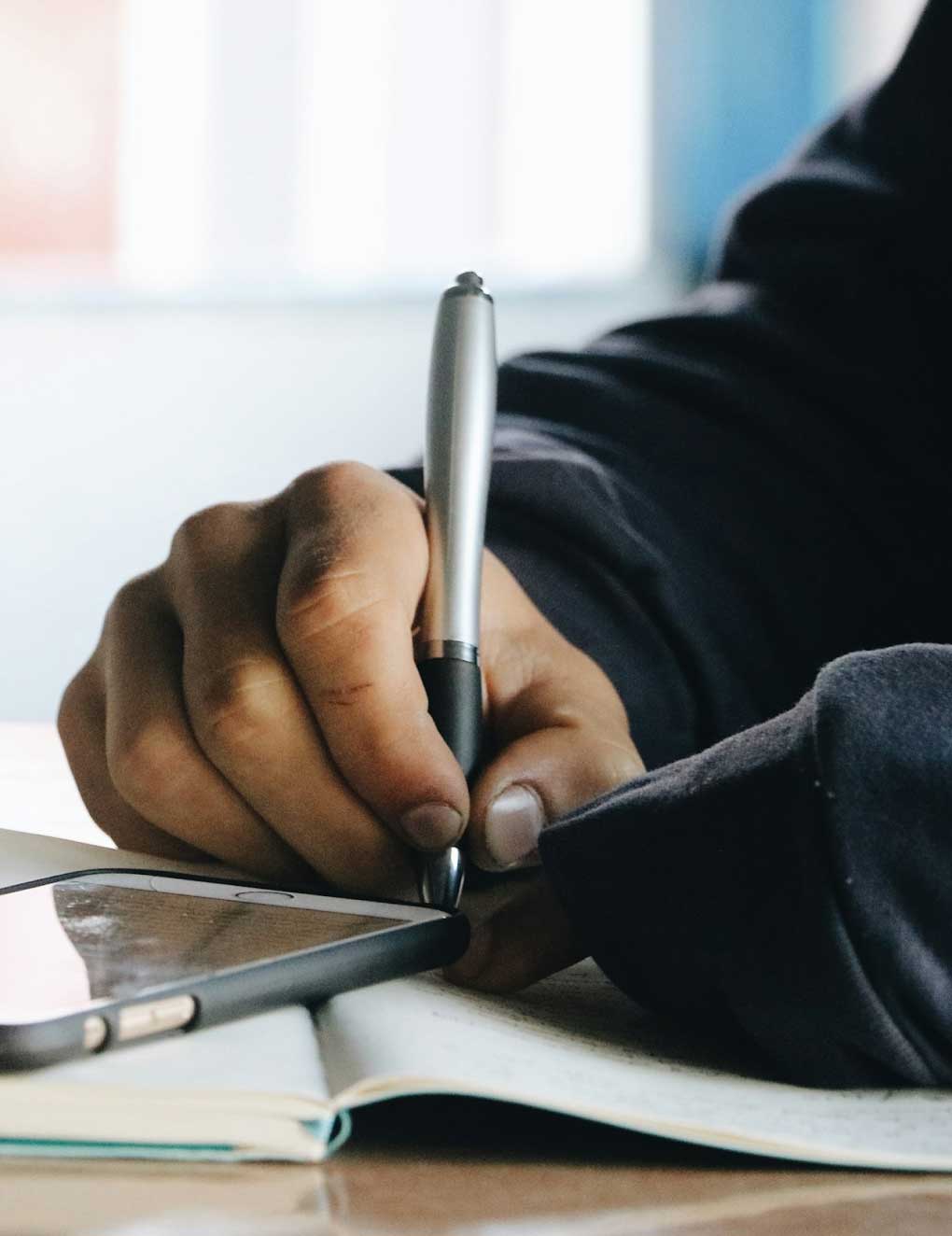 A close-up shot of a person's hand writing something in a notebook.