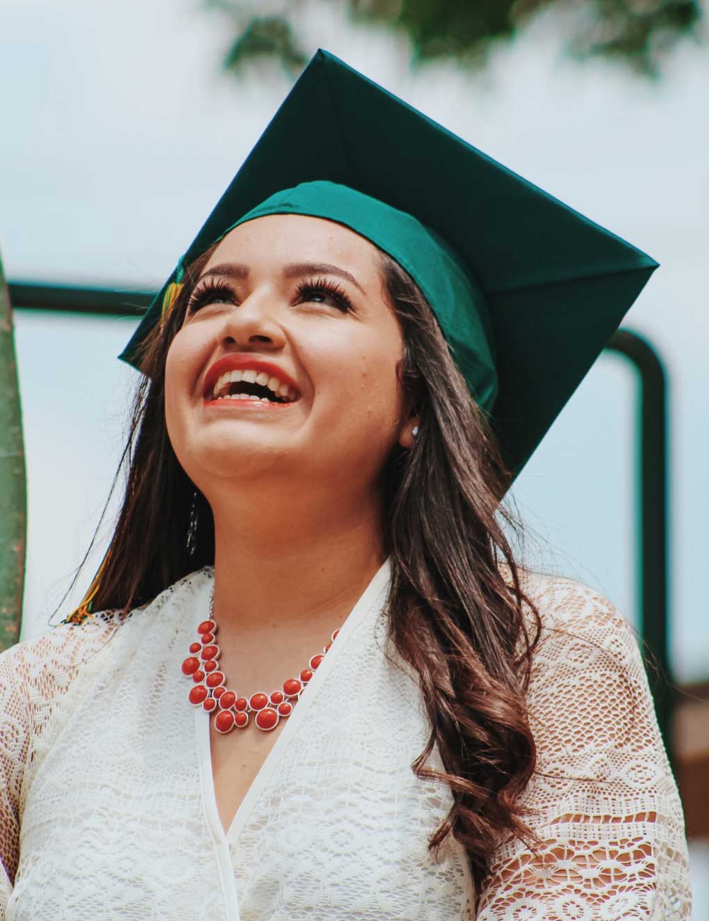 A woman wearing a graduation cap is smiling and looking up at the sky.