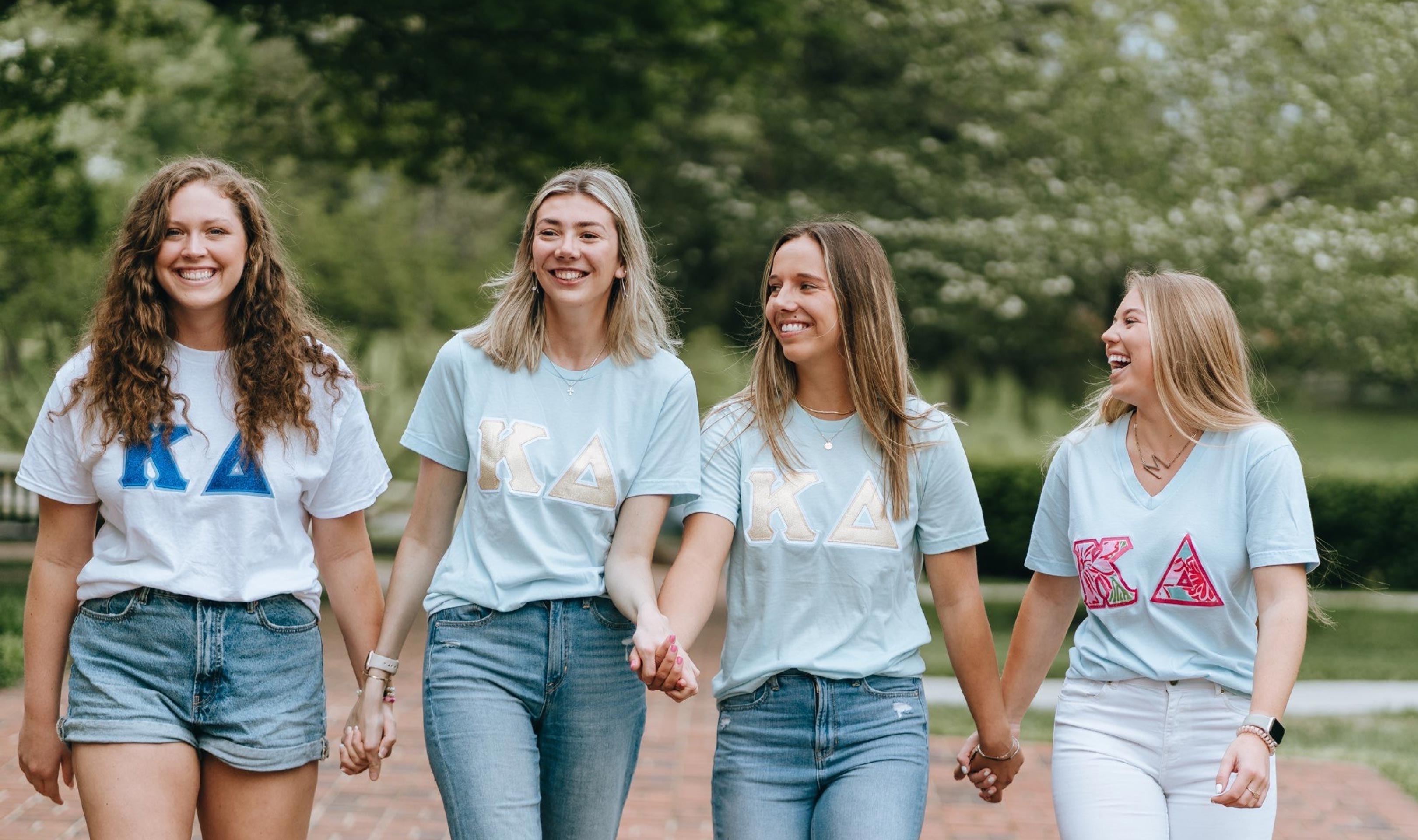 Four women walking toward, looking at each other, and smiling