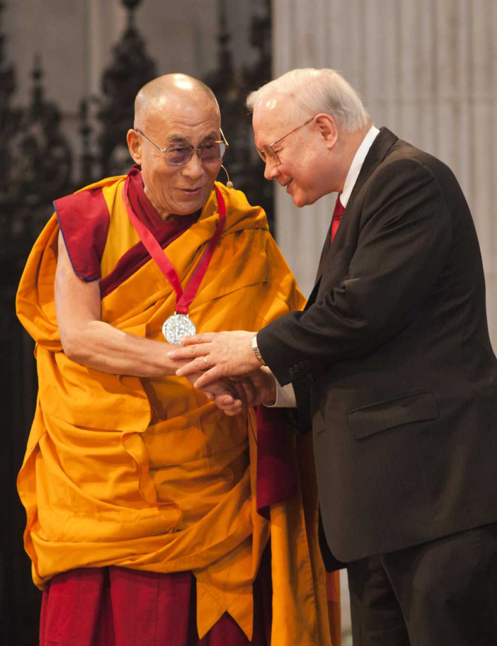 A monk in yellow robes and a man in a suit are shaking hands.