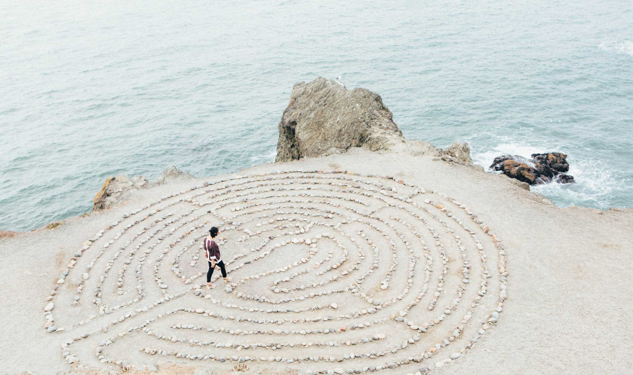 A person is walking among pebbles on the beach, where patterns are drawn with the stones.