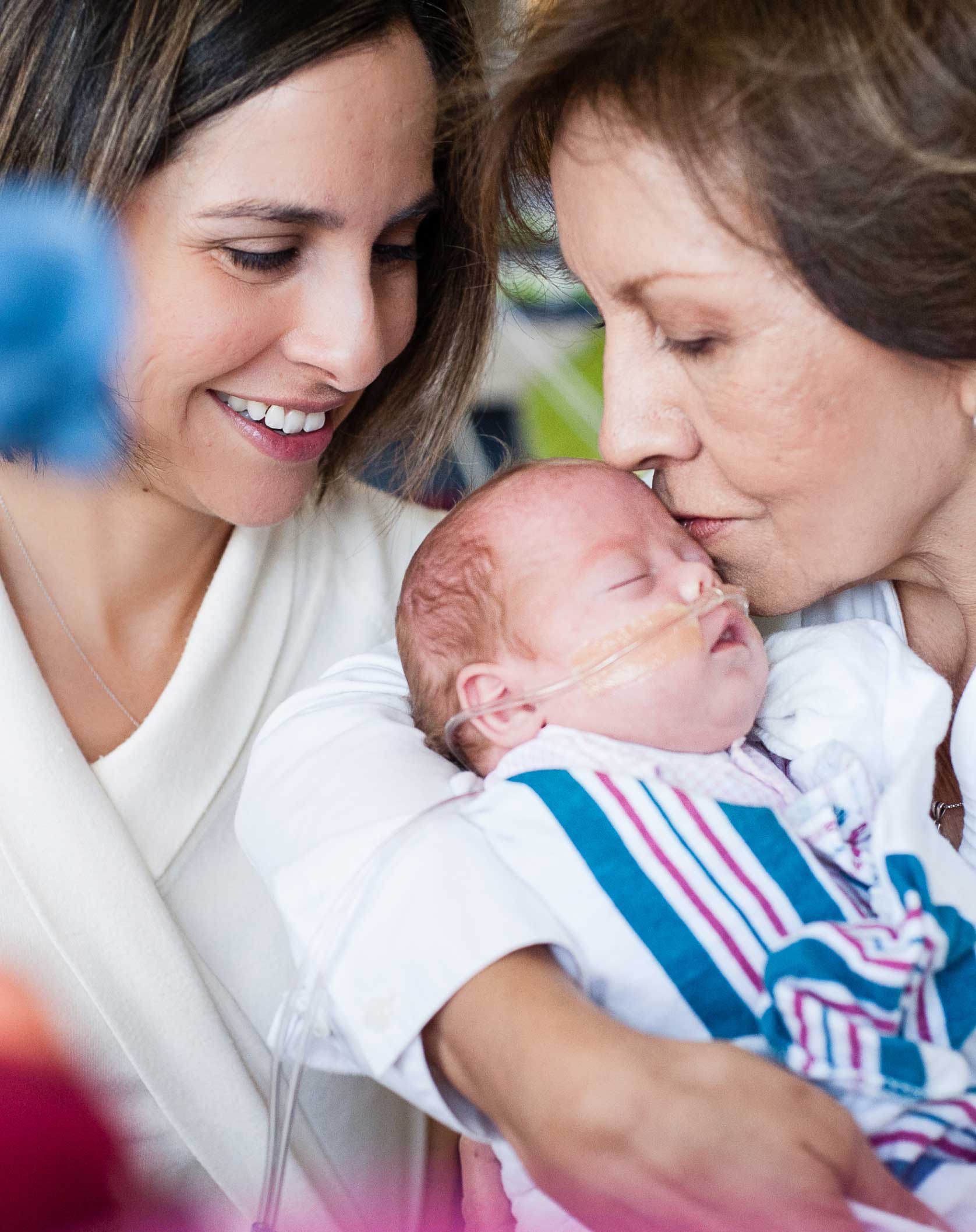 The grandmother is holding the newborn, while the mother is smiling and looking at the newborn.