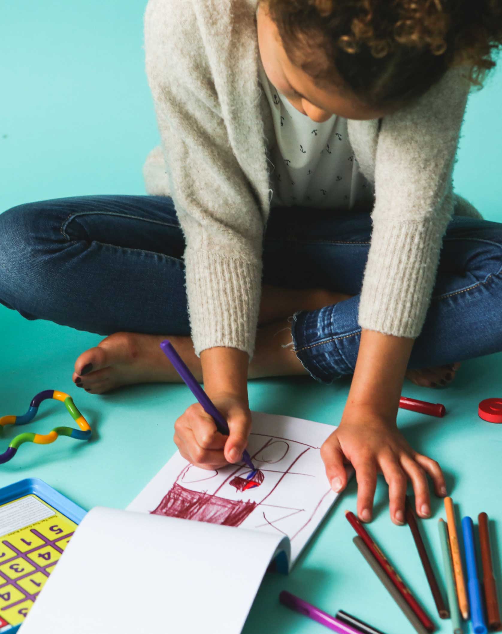 A child is sitting on the floor, drawing in a sketchbook.