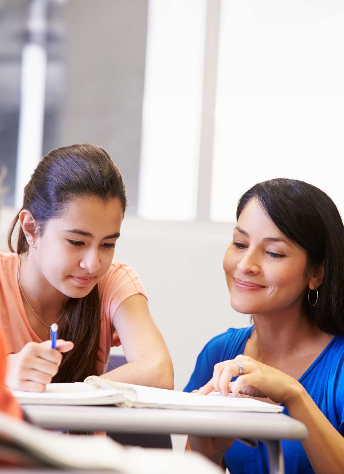 A student and a teacher are smiling while looking at a piece of paper on the desk together at the Knowles teacher initiative